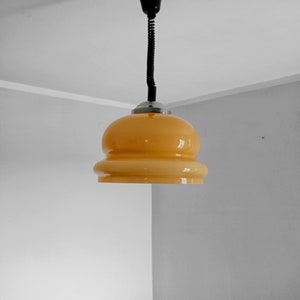 May include: A yellow glass pendant light fixture with a black cord hanging from a white ceiling.