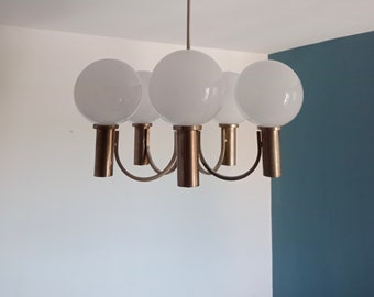 Könnte beinhalten: Ein Messing-Kronleuchter mit fünf weißen, kugelförmigen Leuchten. Der Kronleuchter hat ein schlichtes, modernes Design und hängt an einer weißen Decke.