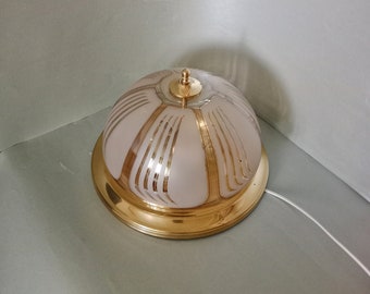 Könnte beinhalten: Eine goldene Deckenleuchte mit einem weißen, mattierten Glasschirm. Der Schirm hat ein geometrisches Muster aus goldenen Linien.