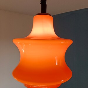 May include: Orange glass pendant light fitting with a rounded, bell-shaped shade.