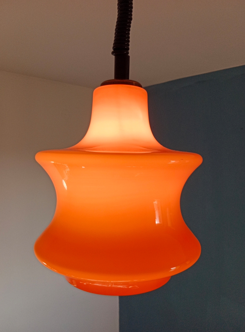 May include: Orange glass pendant light fitting with a rounded, bell-shaped shade.