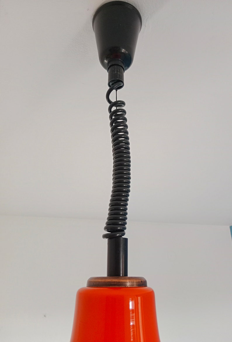 May include: A black ceiling fixture with a coiled cord and an orange glass shade.