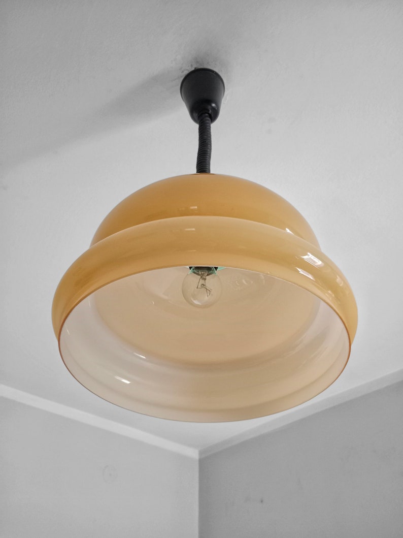 May include: A beige glass pendant light fixture with a black cord and a single light bulb.