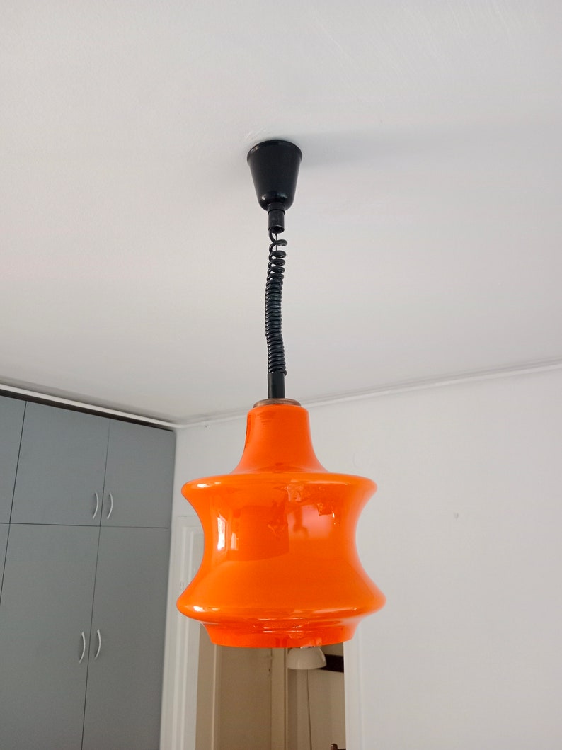 May include: Orange glass pendant light with a black cord and a black ceiling mount.