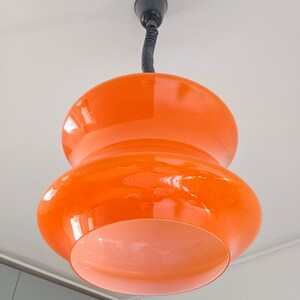 May include: A two-tiered orange glass pendant light fixture with a black cord.