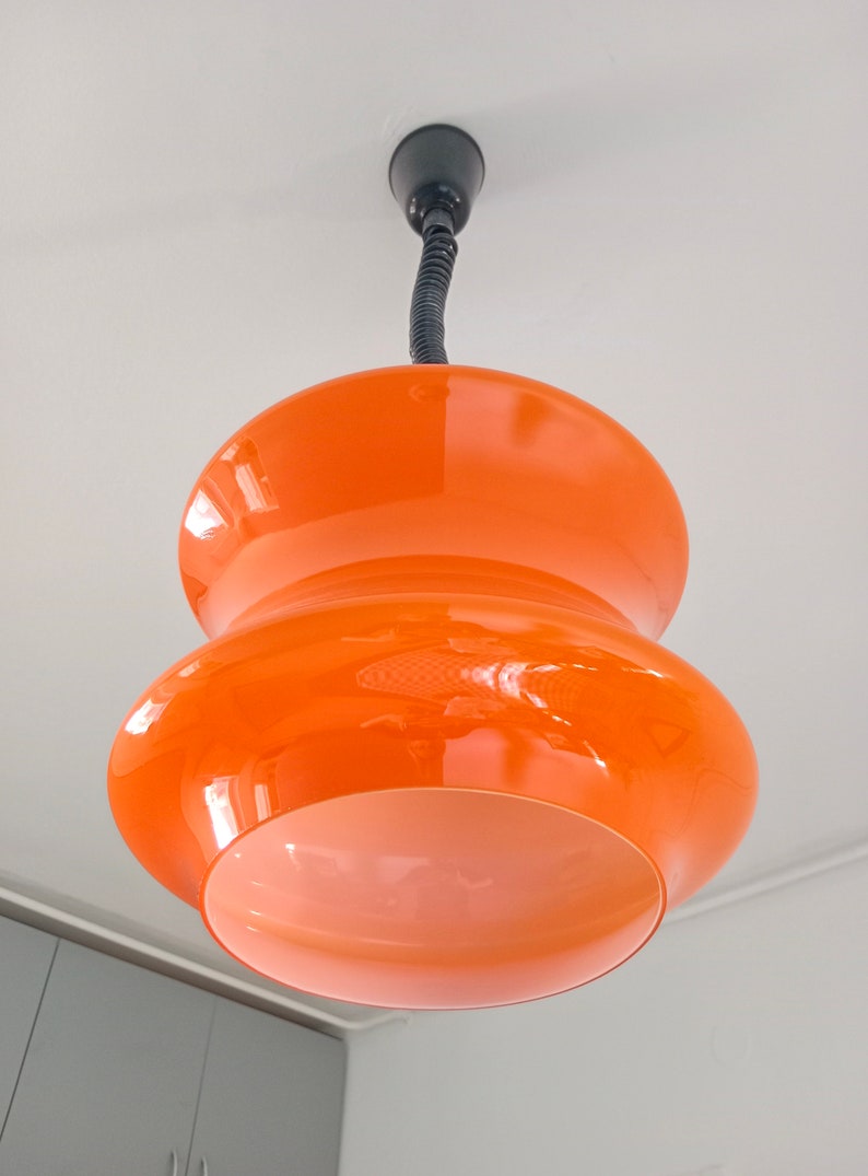 May include: A two-tiered orange glass pendant light fixture with a black cord.