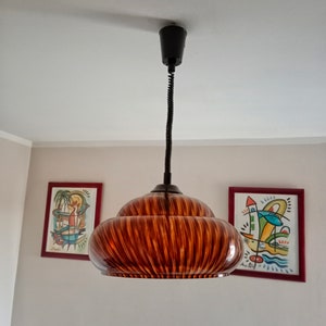 May include: A brown and black striped glass pendant light fixture with a black cord hanging from a white ceiling.