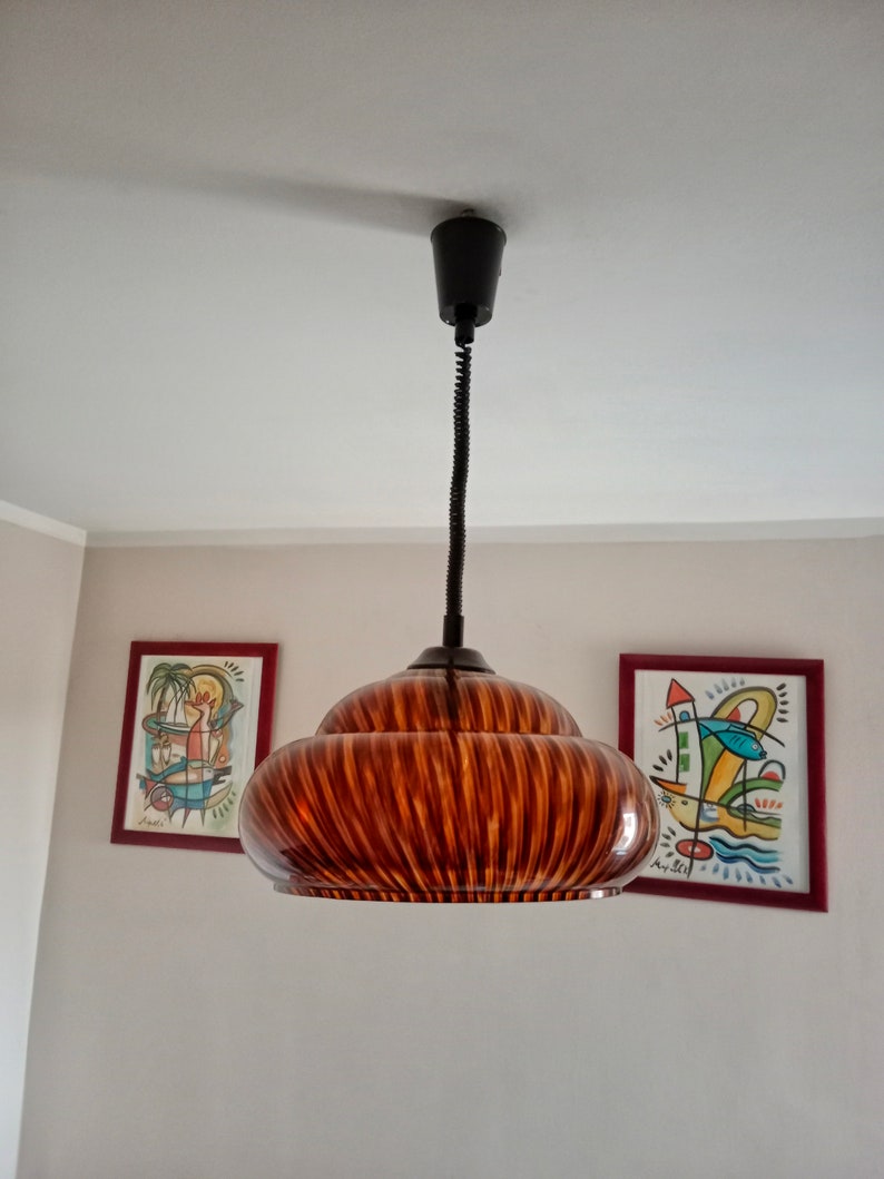 May include: A brown and black striped glass pendant light fixture with a black cord hanging from a white ceiling.