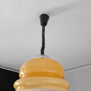 May include: A yellow glass pendant light with a black cord and a black ceiling mount.