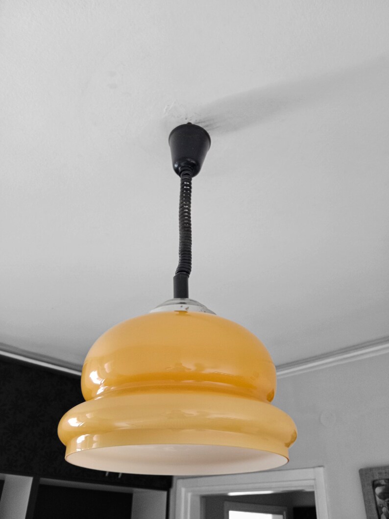 May include: A yellow glass pendant light with a black cord and a black ceiling mount.