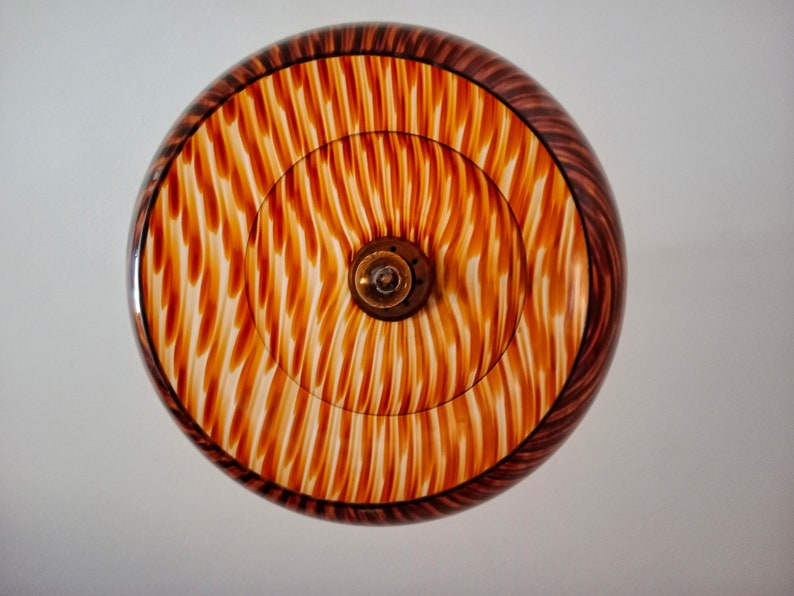 May include: A round, wooden lampshade with a brown and white striped pattern. The lampshade has a central opening for a light bulb.