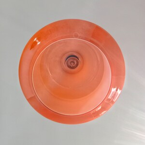 May include: A round, peach-coloured light fixture with a white inner ring and a small, round, silver-coloured light bulb in the centre.