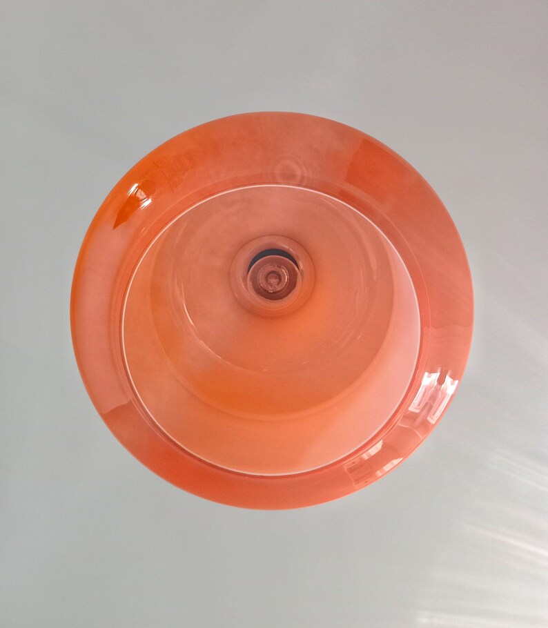 May include: A round, peach-coloured light fixture with a white inner ring and a small, round, silver-coloured light bulb in the centre.