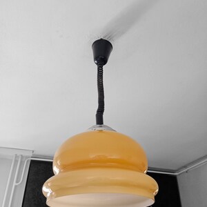 May include: A yellow glass pendant light with a black cord hanging from a white ceiling.