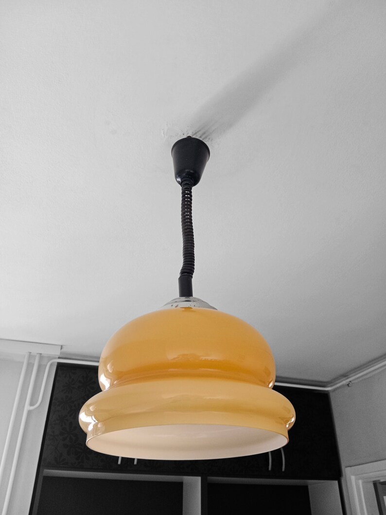 May include: A yellow glass pendant light with a black cord hanging from a white ceiling.