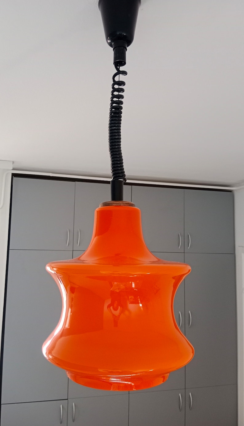 May include: Orange glass pendant light with a black cord and a black ceiling mount.