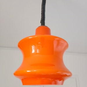 May include: Orange glass pendant light with a black cord and a black ceiling mount.