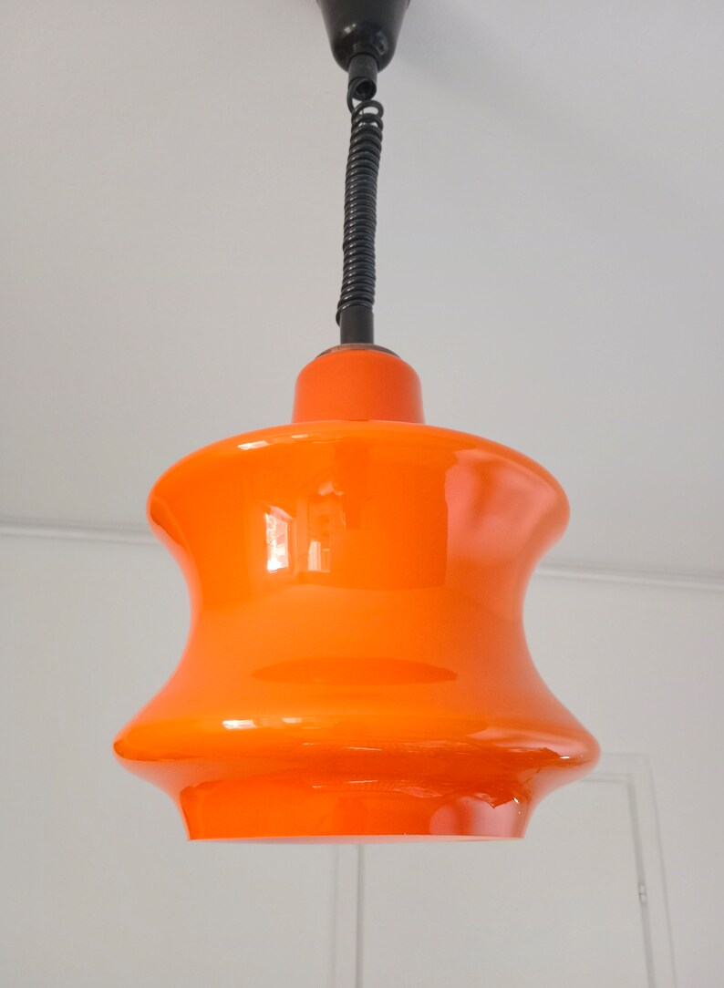May include: Orange glass pendant light with a black cord and a black ceiling mount.