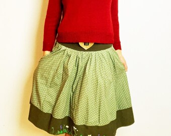 May include: A long-sleeved red knit sweater paired with a gathered green skirt featuring a white polka dot pattern. The skirt has a wide dark green hem decorated with hand-painted floral motifs including small white daisies and purple flowers.