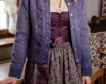 May include: A woman wearing a purple cardigan over a dress. The cardigan has a cable knit design on the sleeves and buttons down the front. The dress is a dark purple with a floral pattern and a satin ribbon belt.