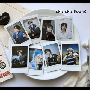 May include: A collection of seven polaroid-style photos featuring young people in various outfits and poses. The photos are arranged on a white plate, with the phrase "chk chk boom!" written above them. A black heart-shaped object is visible in the upper left corner.