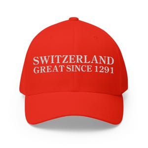 May include: A bright red baseball cap featuring white embroidered text on the front panel. The text reads SWITZERLAND GREAT SINCE 1291 in a clean, capitalized serif font. The cap has a structured crown, a curved brim, and a button on top.