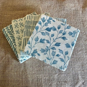 Può includere: Set di quattro sottobicchieri quadrati con diversi motivi blu e bianchi. I sottobicchieri sono realizzati in un materiale naturale come il sughero o la carta e hanno un aspetto rustico.