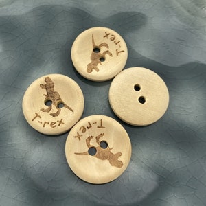 Könnte beinhalten: Vier Holz-Knöpfe mit einer Dinosaurier-Silhouette und dem eingravierten Text "T-Rex". Zwei der Knöpfe haben zwei Löcher, einer hat vier Löcher.