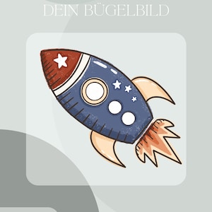 Op de afbeelding: Een cartoon-raketillustratie in blauw, rood en wit, met sterdetails. De afbeelding bevat de tekst "DEIN BÜGELBILD" en "Inklusive Anleitung und Test-Bügelbild".