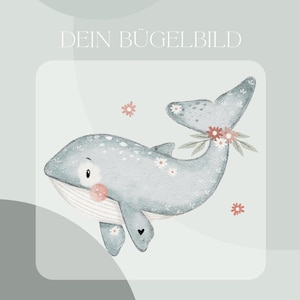 Könnte beinhalten: Aquarell-Illustration eines hellblauen Wals mit weißen Blumenakzenten und einem floralen Schwanz. Der Wal hat eine rosa Wange und ein kleines schwarzes Herz auf seiner Flosse. Der Text "DEIN BÜGELBILD" steht oben.