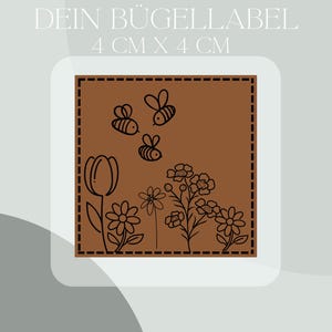 Op de afbeelding: Een bruin vierkant etiket met een bloemen- en bijenontwerp, 4 cm x 4 cm groot. Het etiket heeft een zwarte omtrek van een tulp, madeliefjes en bijen. De tekst "DEIN BÜGELLABEL" staat bovenaan.