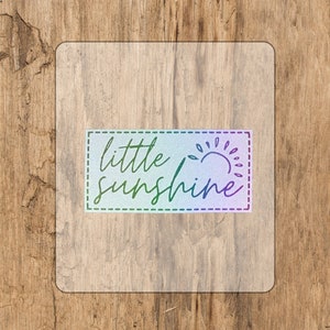 Könnte beinhalten: Ein transparenter Aufkleber mit einem Regenbogen-Farbverlauf. Der Aufkleber hat einen weißen Hintergrund mit dem Text "little sunshine" und einer stilisierten Sonnengrafik.
