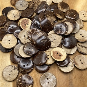 Könnte beinhalten: Ein Haufen brauner und natürlicher Kokosnussschalenknöpfe mit jeweils zwei Löchern. Die Knöpfe sind in einem zufälligen Muster auf einer Holzoberfläche angeordnet.