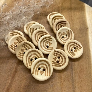 Puede incluir: Un conjunto de 10 botones de madera con un diseño de arcoíris y corazón. Los botones son de color marrón claro y tienen un acabado de madera natural.