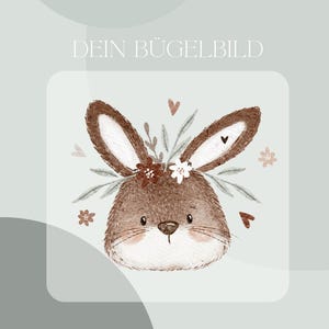 Puede incluir: Un conejito marrón con una corona floral, adornada con flores blancas y rosas, sobre un fondo azul claro. El texto "DEIN BÜGELBILD" está en la parte superior de la imagen. El texto "Inklusive Anleitung und Test-Bügelbild" está en la parte inferior de la imagen.