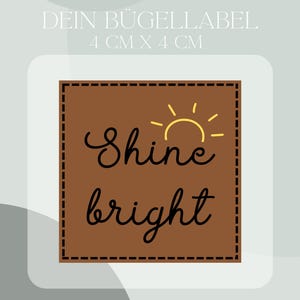 May include: Brown iron-on label with a stitched border. The label features a yellow sun graphic and the text "Shine bright" in black cursive font. The label measures 4 cm by 4 cm.