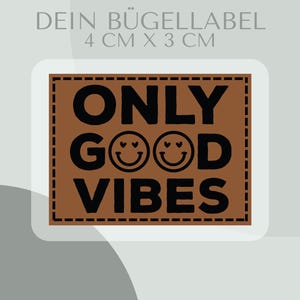 Könnte beinhalten: Ein brauner Aufbügler mit dem Text "ONLY GOOD VIBES" in Schwarz. Der Aufbügler ist 4 cm x 3 cm groß und hat einen gestickten Rand. Das Wort "GOOD" hat zwei Smiley-Emojis. Der Text "DEIN BÜGELLABEL" steht oben.