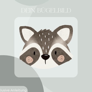 Peut inclure: Un visage de raton laveur de dessin animé avec un nez noir, des joues roses et des accents blancs. Le texte "DEIN BÜGELBILD" est en haut et "Inklusive Anleitung und Test-Bügelbild" en bas. Le raton laveur est sur fond bleu clair.