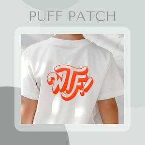 Può includere: Maglietta bianca con una toppa in rilievo rossa "WTF!" sul retro.