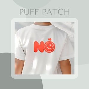 Könnte beinhalten: Weißes T-Shirt mit rotem "Nö" Smiley-Puff-Patch-Design auf dem Rücken. Das Shirt hat kurze Ärmel und einen Rundhalsausschnitt. Der Text "PUFF PATCH" befindet sich oben im Bild.