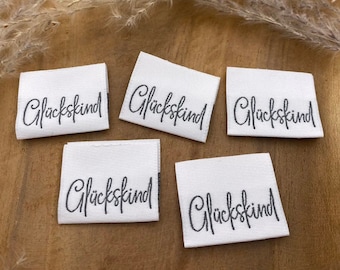 May include: Five white fabric labels with the word "Glückskind" written in black cursive script.