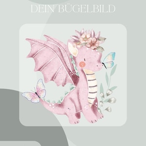 May include: A pink dragon illustration with a flower crown and butterflies. The dragon has large wings and a striped belly. Text at the top reads "DEIN BÜGELBILD" and at the bottom "Inklusive Anleitung und Test-Bügelbild".
