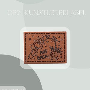 Könnte beinhalten: Ein braunes rechteckiges Patch mit einer Raketenillustration und dem Text "TO THE MOON AND BACK!". Das Patch hat einen gepunkteten Rand und Sternakzente. Der Text "DEIN KUNSTLEDERLABEL" steht oben.