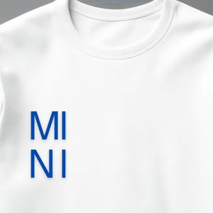 Puede incluir: Sudadera blanca de cuello redondo con el texto azul "MI NI" alineado verticalmente en la parte delantera. La sudadera tiene un dise&ntilde;o cl&aacute;sico y minimalista, adecuado para ropa casual. La tela parece suave y c&oacute;moda.
