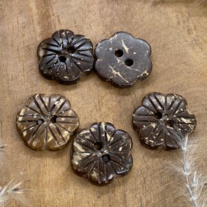 May include: Five brown coconut shell buttons with a flower shape and two holes. The buttons have a natural, rustic look.