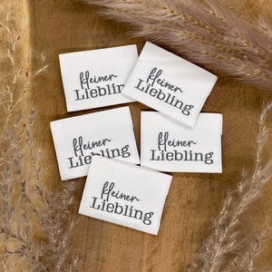 May include: Five white fabric labels with black text that reads "kleiner Liebling" which translates to "little darling" in English.