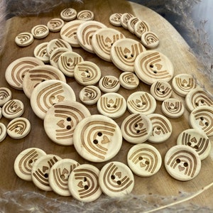May include: A collection of wooden buttons featuring a rainbow and heart design. The buttons are light brown and have a natural wood finish.