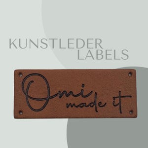 Könnte beinhalten: Braunes Leder-Etikett mit dem Text "Omi made it" in schwarzer Schrift.