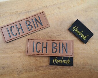 May include: Two brown leather patches with the text "ICH BIN" in black lettering.  Two black fabric patches with the text "Handmade" in gold lettering.
