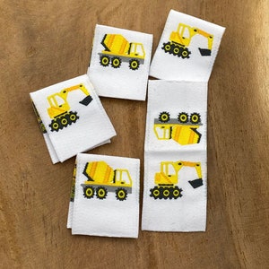 May include: Six white fabric labels with yellow and black embroidered images of construction vehicles. The labels feature a cement mixer and an excavator.